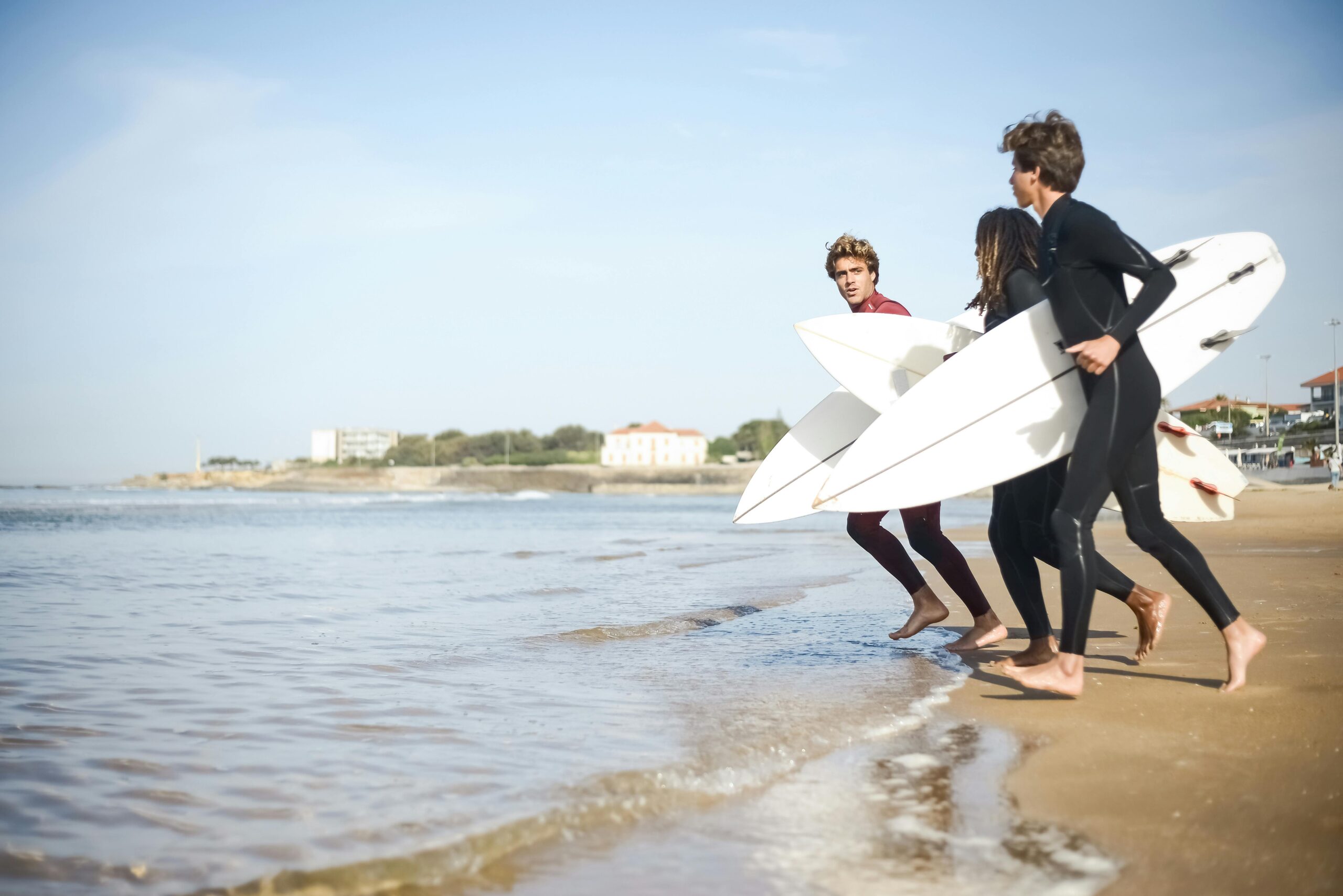 Ludzie wbiegający do wody trzymając pod pachami deski surfingowe