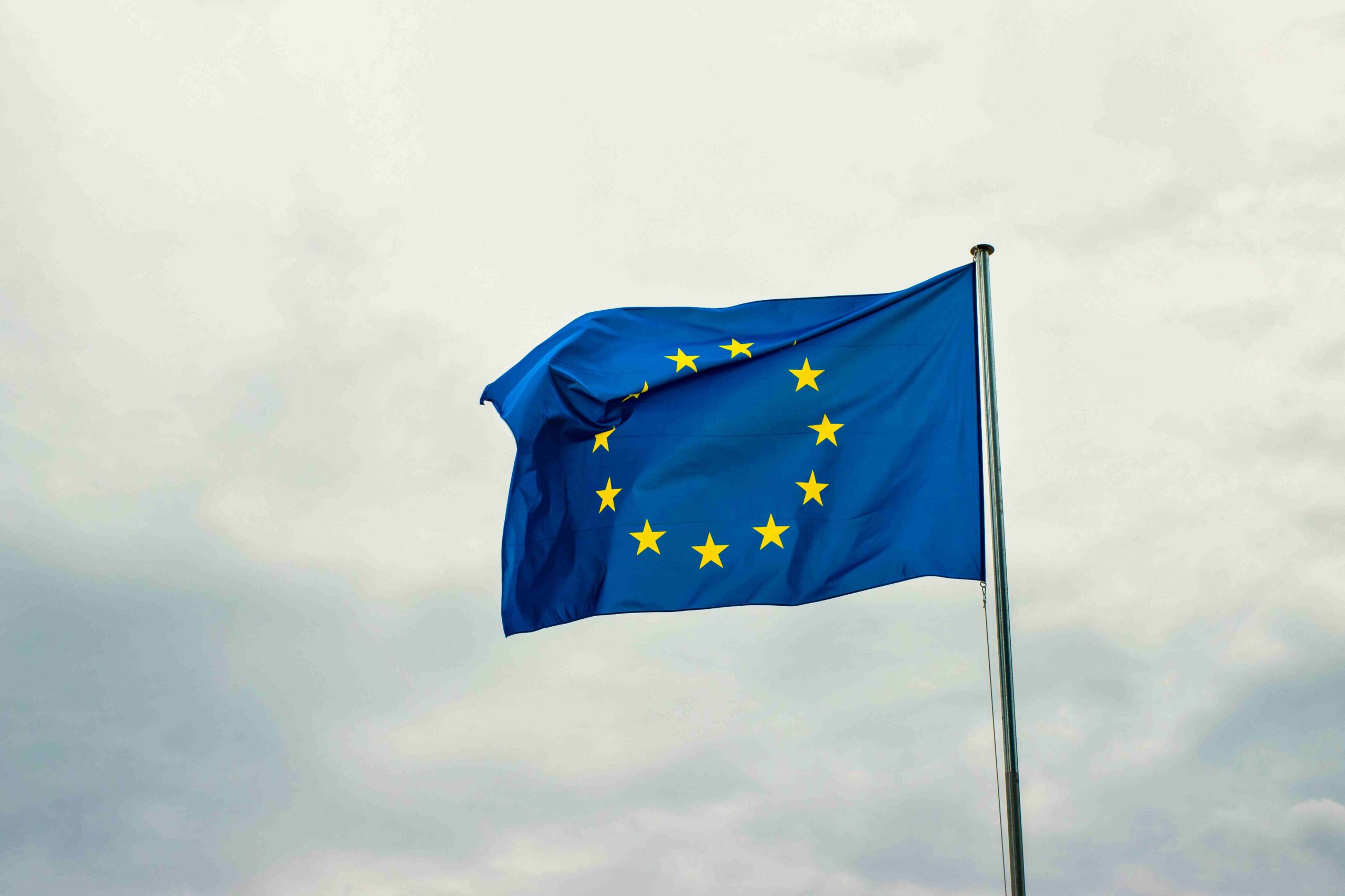 Kto będzie musiał raportować w ESG po zmianach w przepisach ESG? Flaga Unii Europejskiej powiewająca na wietrze na tle pochmurnego nieba.